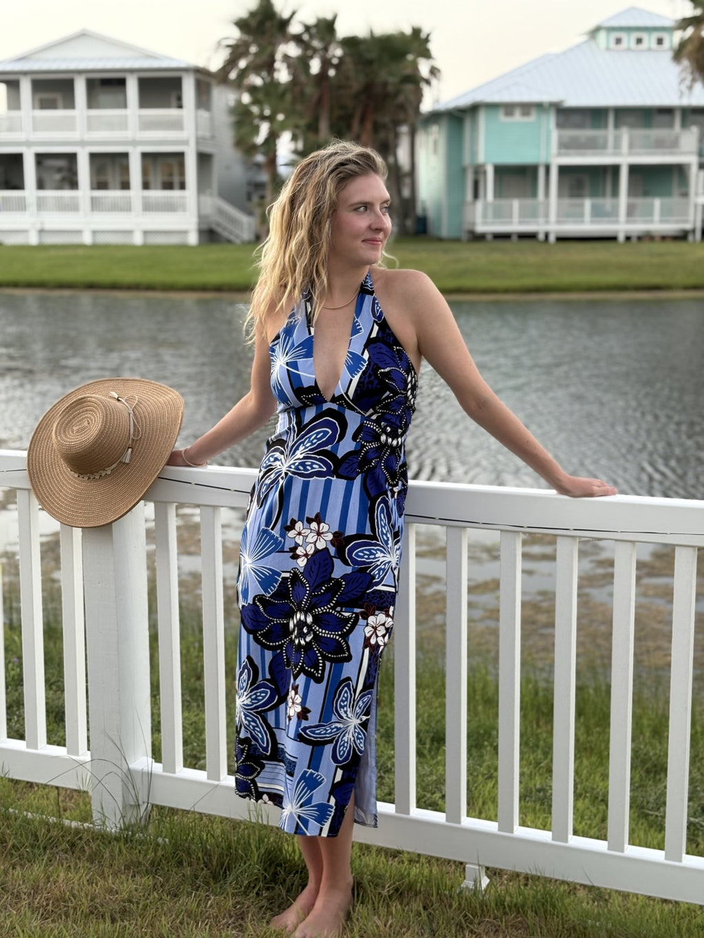 Woman in blue multi halter-style dress by the water, perfect for tropical vacations and coastal boutique clothing.