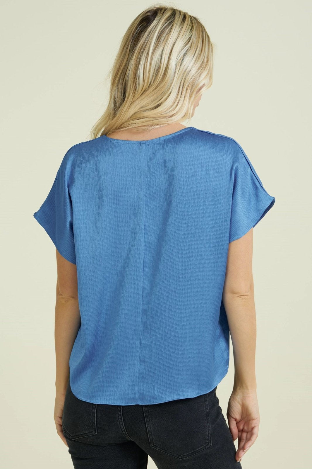 Back view of a woman wearing a BLUE TEXTURED SATIN TOP from Raggdoll Boutique, showcasing trendy coastal style.