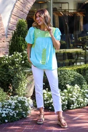 A woman wearing THE COVE TOP from Raggdoll Boutique, paired with white pants, perfect for coastal fashion.