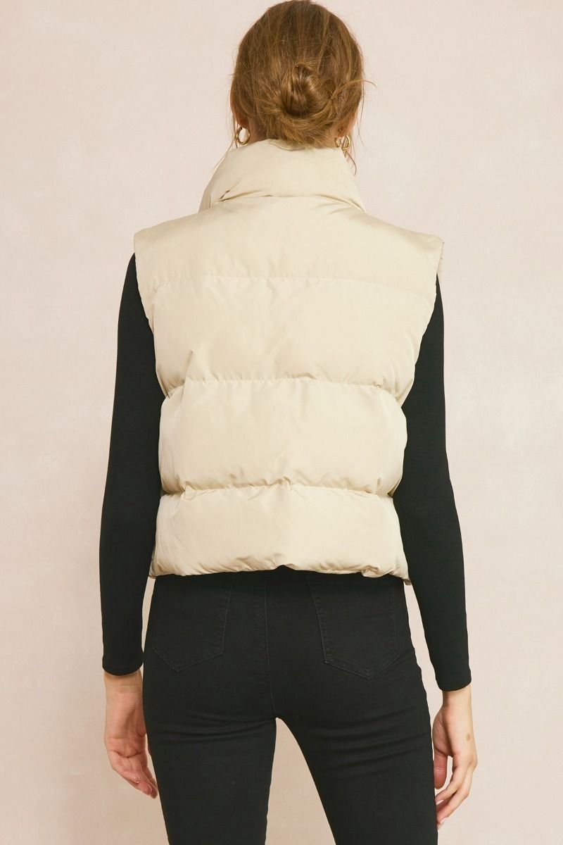 Back view of a woman wearing a PUFFER VEST SANDSTONE from Raggdoll Boutique, perfect for trendy coastal style.