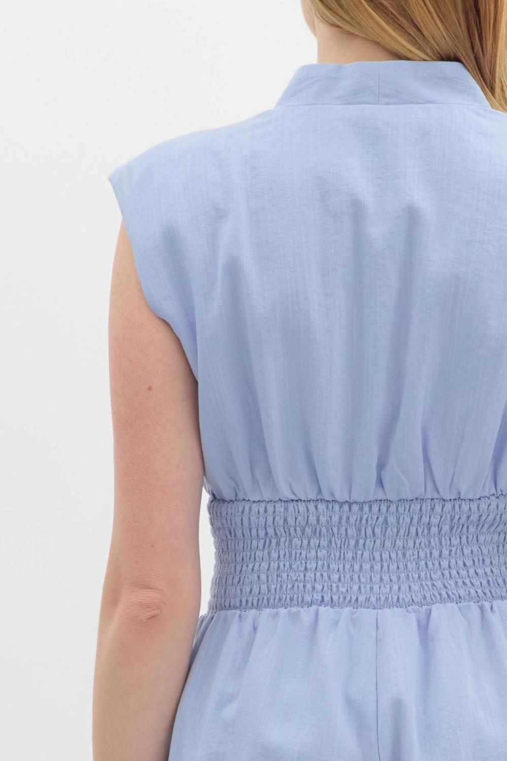 Back view of a light chambray jumpsuit with smocked waist, ideal for coastal boutique clothing and stylish summer events.