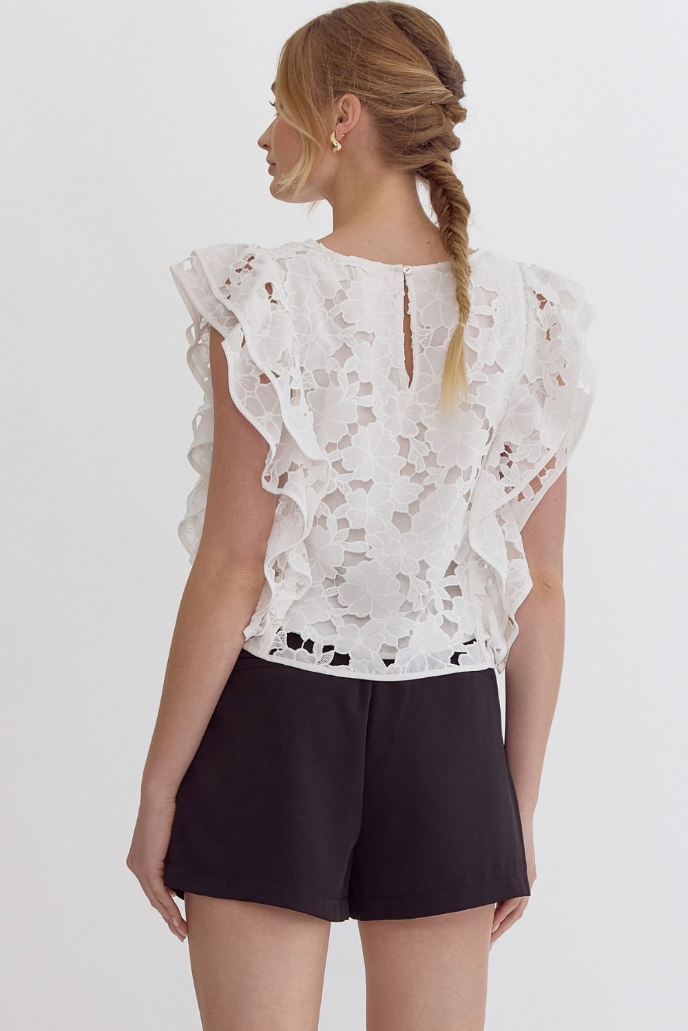 Back view of a woman wearing a White Lace Cut-Out Top paired with black shorts, showcasing trendy coastal style.