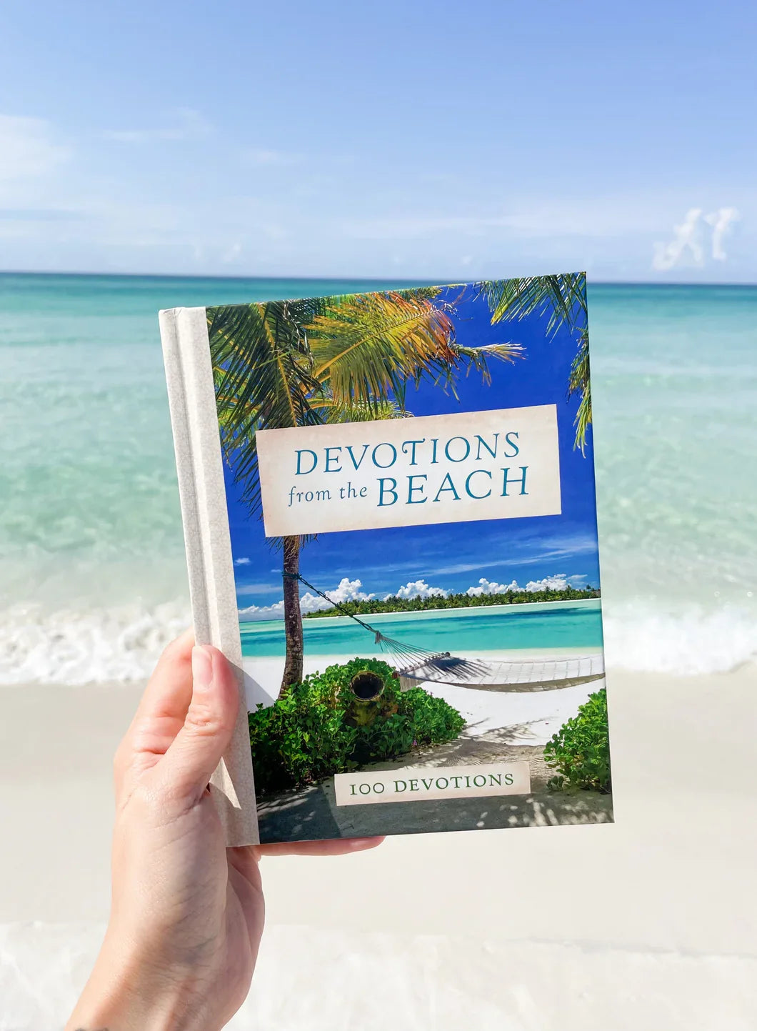 Person holding 'Devotions from the Beach' book against a tropical beach background.