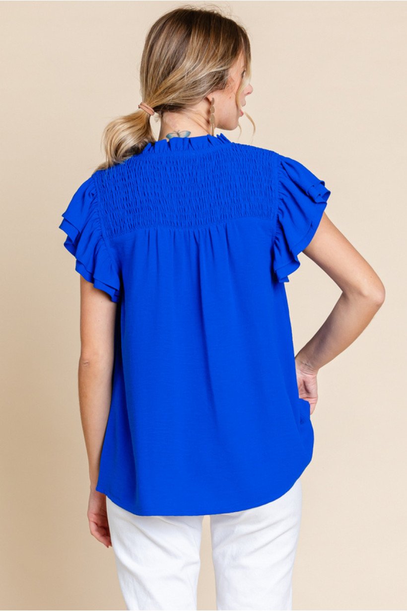 Back view of a woman wearing a blue Royal Smocked Top from Raggdoll Boutique, showcasing trendy coastal style.