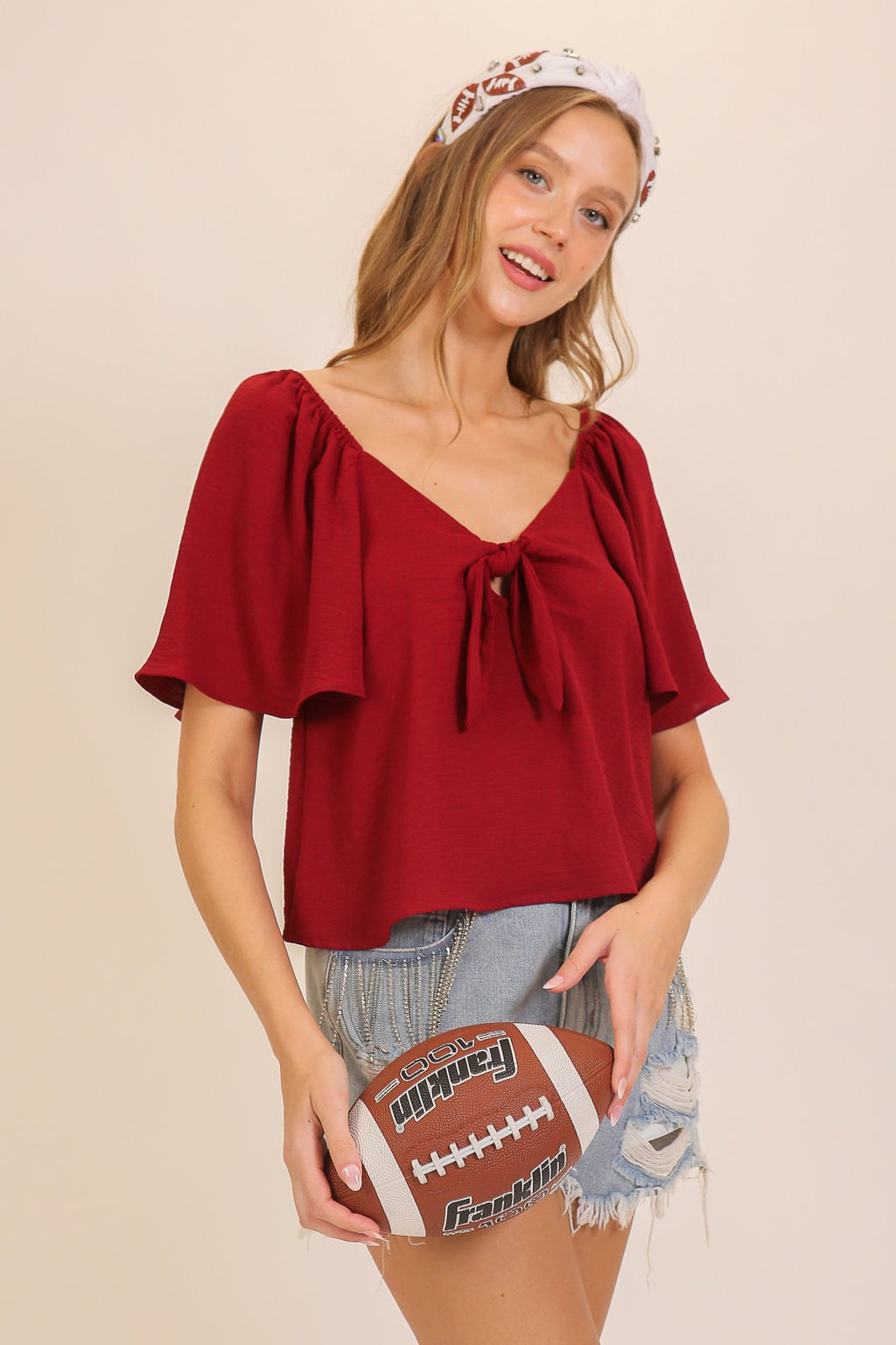 Model wearing a maroon game day top with tie detail, styled for coastal boutique clothing and perfect for tropical vacations.