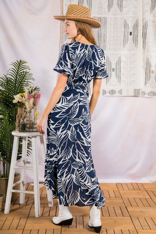 Woman wearing SUN KISSED MIDI IN NAVY dress with tropical leaf print, stylish coastal fashion from Raggdoll Boutique.
