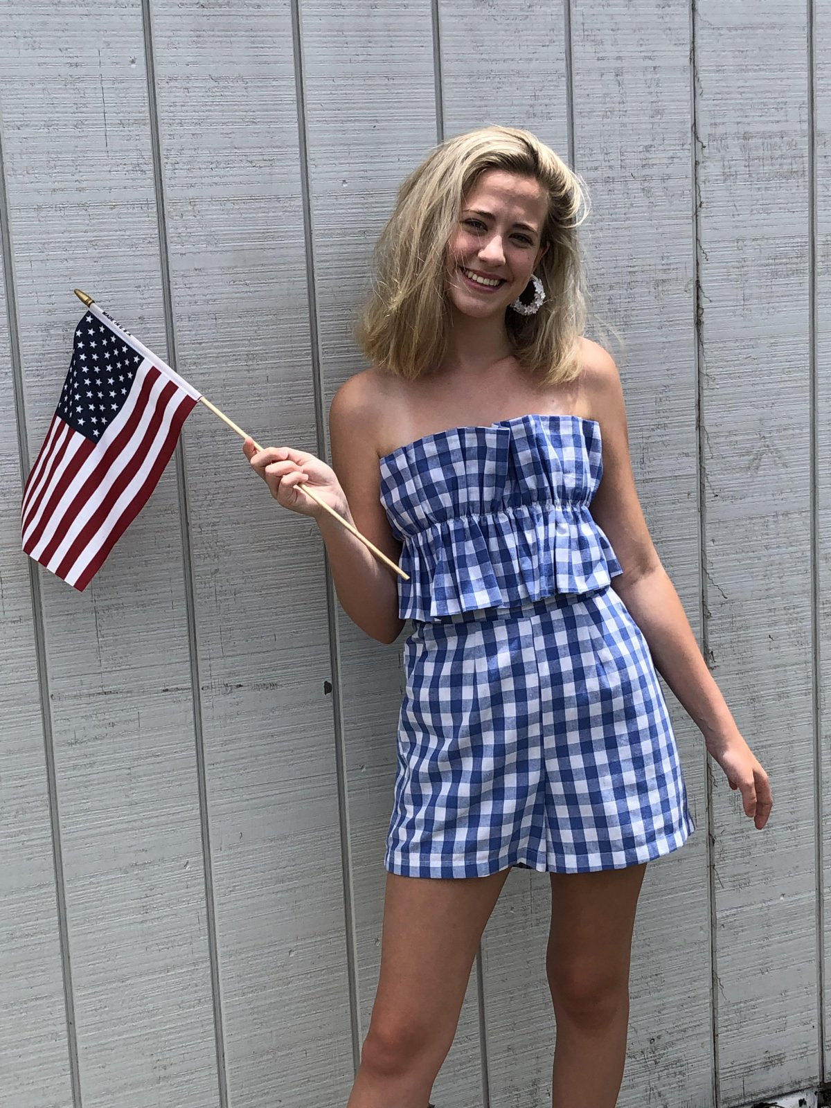 CHECK IT OUT ROMPER with blue and white checks, ruffle front, model holding flag, Raggdoll Boutique.