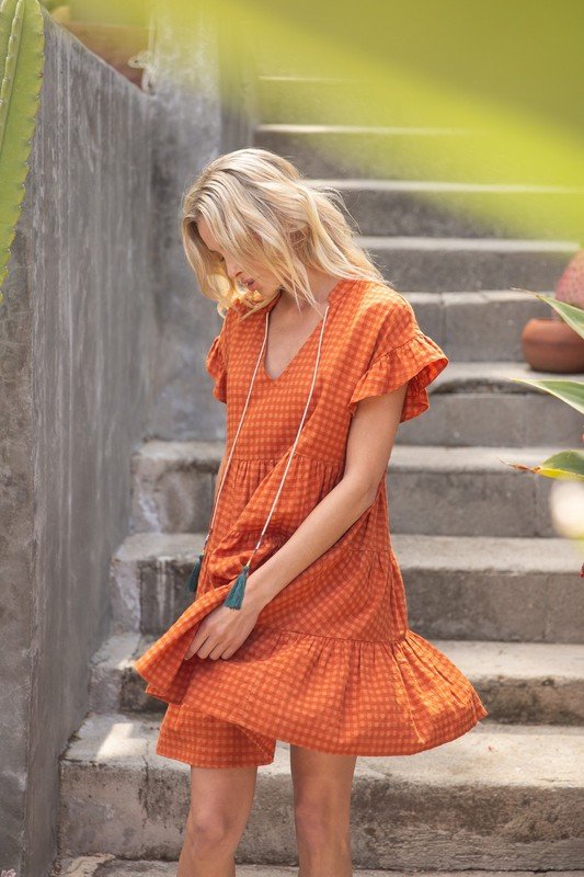 SWEET BABY DOLL DRESS worn by a woman on stairs, featuring tiered style, deep V neckline, and tassel details.