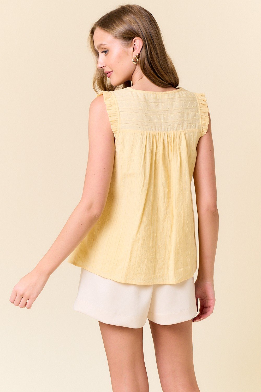 Pastel yellow ruffled tank top from a coastal boutique, perfect for tropical vacations and casual outings.
